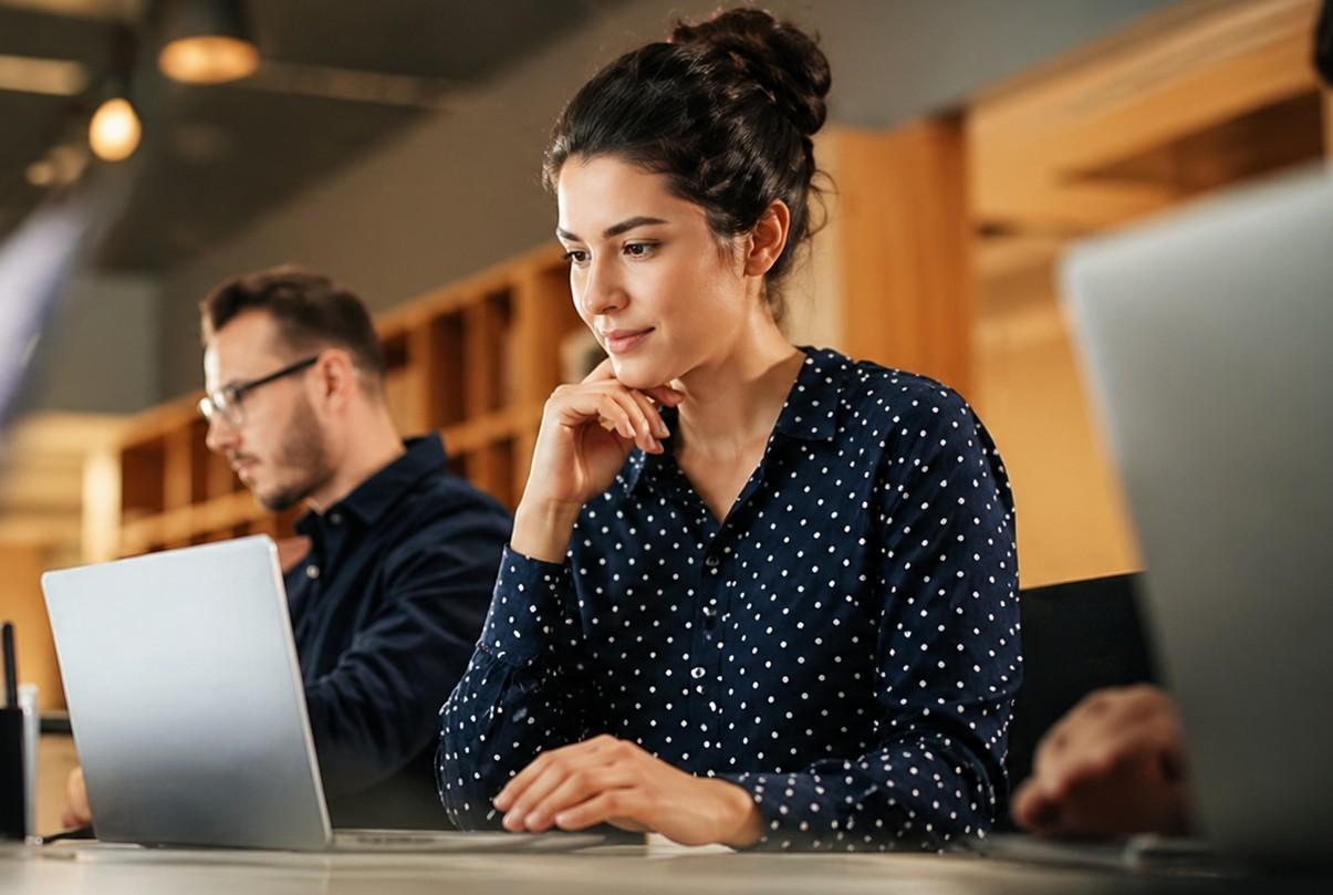 A professional woman working on a laptop in an office setting, concentrating to improve her performance at work
