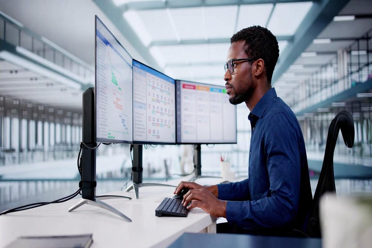 Professional man working at a multi-monitor computer setup in a modern office, representing new collar jobs in 2026